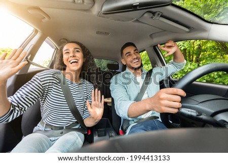 Emotional millennial mixed race couple handsome arab guy and pretty brunette lady having fun while car trip, listening to music and cherfully singing, shot from inside the auto, sun flare Royalty-Free Stock Photo #1994413133