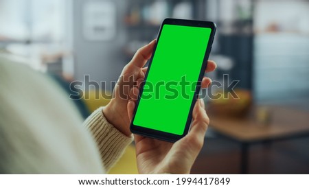 Close Up of an Authentic Female Using Smartphone with Green Screen Mock Up Display at Home Living Room while Lying on a Couch Sofa. She's Browsing the Internet and Checking Videos on Social Networks.