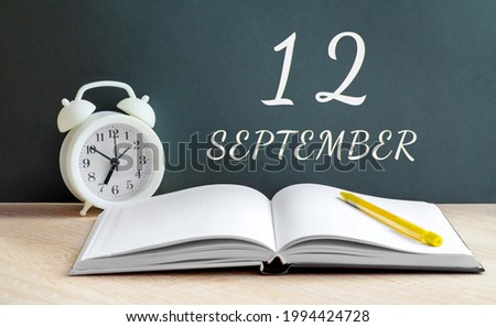 september 12. 12-th day of the month, calendar date.A white alarm clock, an open notebook with blank pages, and a yellow pencil lie on the table. Autumn month, day of the year concept.