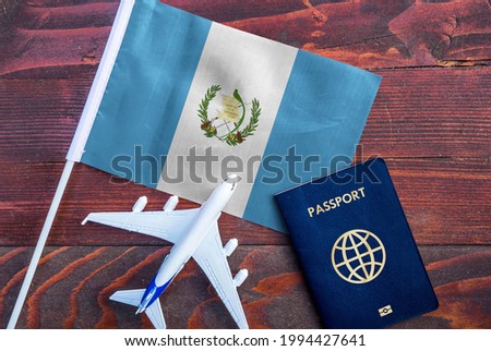 Flag of Guatemala with passport and toy airplane on wooden background. Flight travel concept 