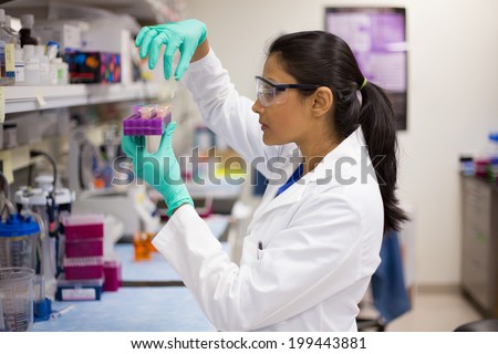 Closeup portrait, young scientist in labcoat wearing nitrile gloves, doing experiments in lab, academic sector. Royalty-Free Stock Photo #199443881