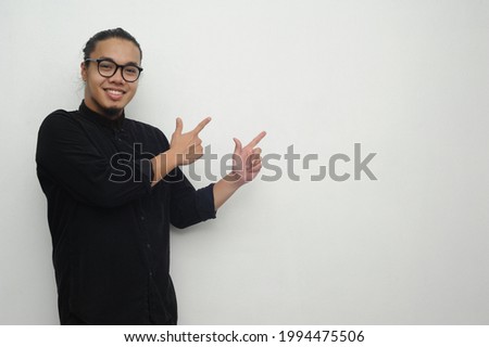 Cheerful handsome asian man looking excitedly at camera and pointing with fingers away on empty white background  
