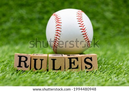 Baseball with word RULES are on green grass