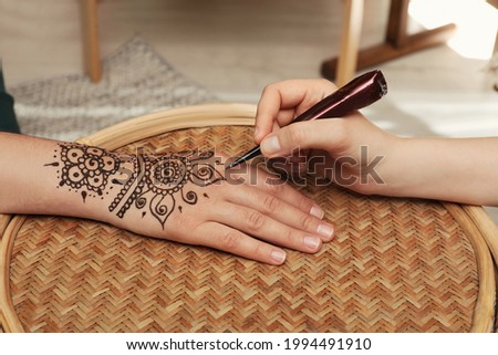 Master making henna tattoo on hand at table, closeup. Traditional mehndi
