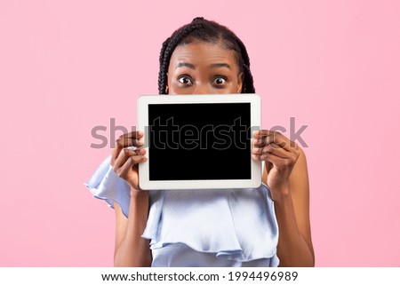 Millennial African American lady hiding behind tablet pc with blank screen on pink studio background, mockup for app or website. Online life, education, communication concept