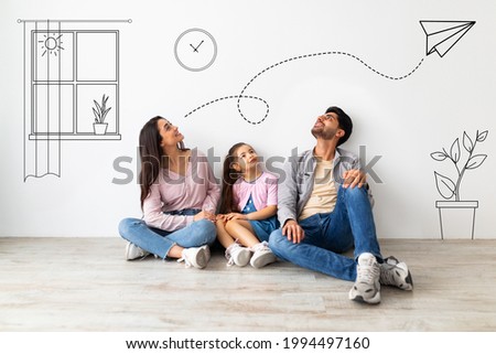 Young family of three imagining interior of their new flat, sitting on floor near white wall with doodle drawings, planning relocation. Creative collage with illustrations on background Royalty-Free Stock Photo #1994497160
