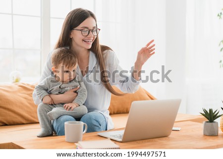 Happy young single mother having video call conference online on laptop holding toddler newborn baby infant talking with a pediatrician grandparents doctor colleagues working from home on freelance