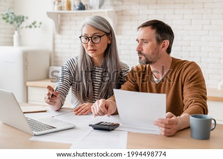 Mature middle-aged couple family wife and husband counting funds, savings declarations, investments,paperwork, financial documents, bankruptcy, court case, bills, pension with laptop. Royalty-Free Stock Photo #1994498774