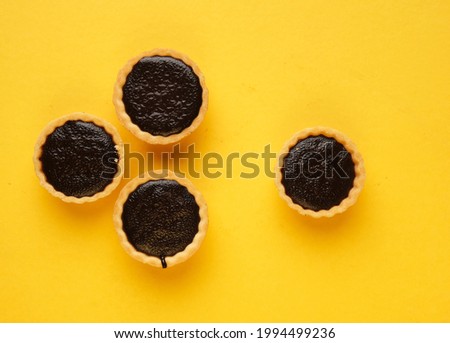 A picture of four homemade chocolate tart on yellow background. Same colour subject and background concept