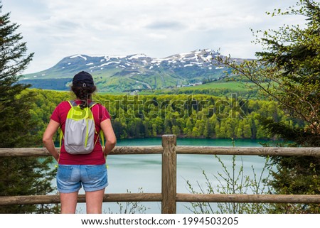 Young woman (unrecognizable back view) admiring view of lake Pavin in Auvergne Volcanic Regional Nature Park, France.  Active holidays in nature background. Travel, natural lifestyle concepts.