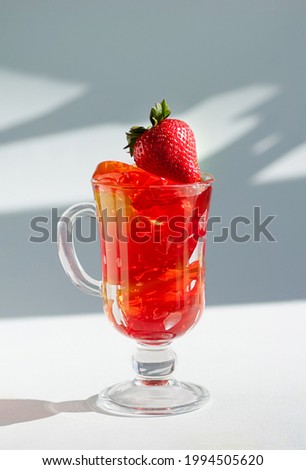Ripe strawberries and delicious fruit jelly in a glass glass on a white background. Vertical crop. Close up.