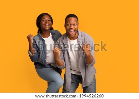 Big Win. Happy Excited Black Couple Celebrating Success With Raised Fists, Cheerful African American Man And Woman Exclaiming With Joy While Standing Isolated Over Yellow Background, Copy Space Royalty-Free Stock Photo #1994526260