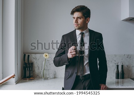 Young thoughtful minded successful employee business man corporate lawyer 20s in formal black suit shirt tie drink coffee breakfast look aside in light kitchen Achievement career lifestyle concept. Royalty-Free Stock Photo #1994545325