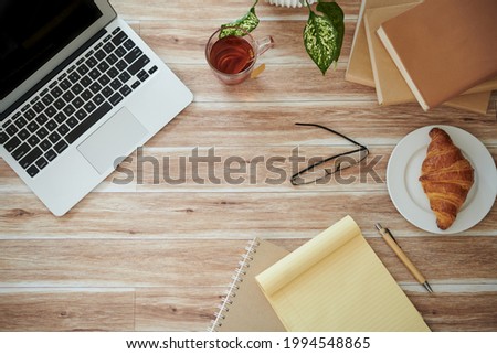 Desk of student with opened laptop, books, planner, cup of tea and croissant
