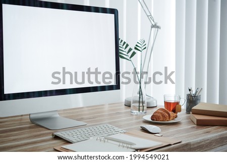 Empty computer monitor, opened planner, croissant on plate and stack of books on desk of university student