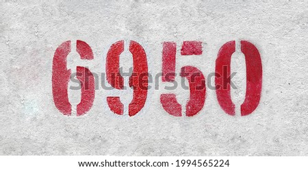 Red Number 6950 on the white wall. Spray paint. Number six thousand nine hundred fifty.