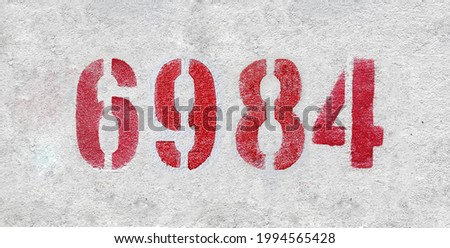 Red Number 6984 on the white wall. Spray paint. Number six thousand nine hundred and eighty four.