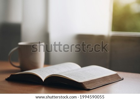 Open bible with a cup of coffee for morning devotion on wooden table with window light.book and coffee cup on wooden table. Royalty-Free Stock Photo #1994590055