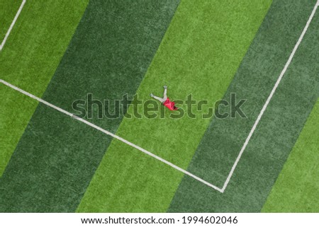 Aerial top view of a child lying on the lawn of a football field