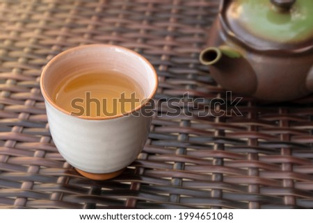 White ceramic cup with healthy herbal tea and teapot on background with warm cozy atmosphere