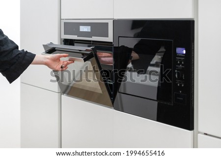 Woman holding black built in electric ovens door with orange light inside, checking if her chocolate pie is ready, cooking food using kitchen appliances, preparing dessert Royalty-Free Stock Photo #1994655416