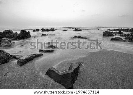Beach Sunrise with slow shutter speed mode on camera for water smooky effet. Beach with lots of rocks and waves in black and white