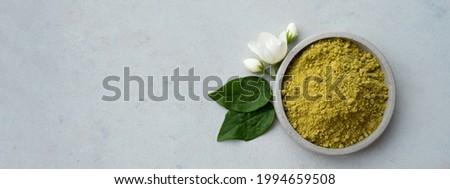 Banner. henna powder for dyeing hair and eyebrows and drawing mehendi on hands on a gray cement pedestal with dried flowers or a white flower.