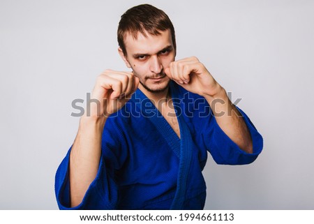 Young man in a blue kimono on a white background. The guy is new to martial arts. studio photo