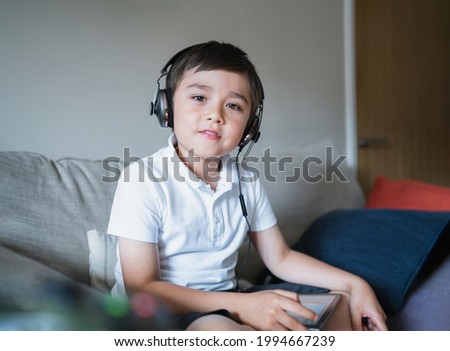 Kid wearing headphone listening to music,Child boy doing homework by using digital tablet searching information on internet,E-learning, New normal life,Children with social network concept
