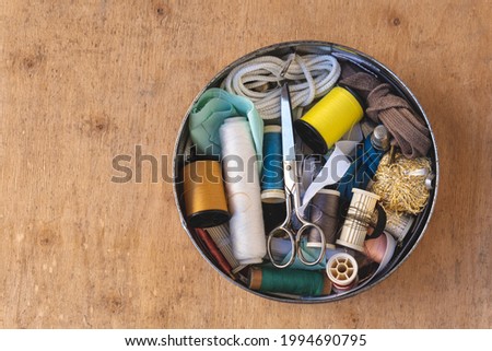 Round brass box, with sewing utensils, on a wooden background.  Royalty-Free Stock Photo #1994690795