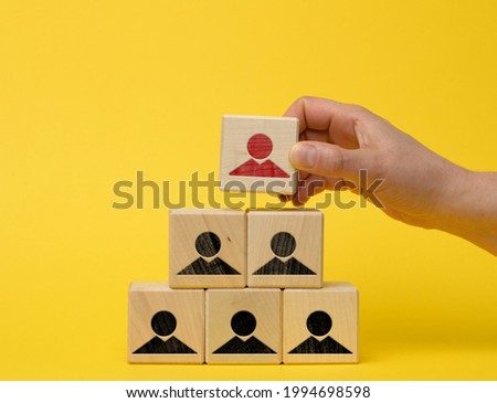female hand holds a wooden block on a blue background. Recruitment concept, teamwork, effective management. CEO search, yellow background