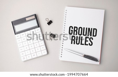 The word GROUND RULES is written on a white background next to a pen ,calculator and reports. Business concept