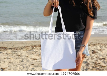 Girl is holding tote bag canvas fabric for mockup blank template isolated on beach and sea background.