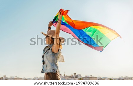 girl with pamela holding pride flag with both hands. girl looks to the horizon and the light is warm. lgtb. concept of equality and tolerance.