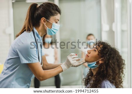 A nurse takes sample from nose of an African American teenager girl to antigen test for coronavirus.