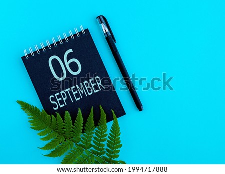 September 6th. Day 6 of month, Calendar date. Black notepad sheet, pen, fern twig, on a blue background. Autumn month, day of the year concept.
