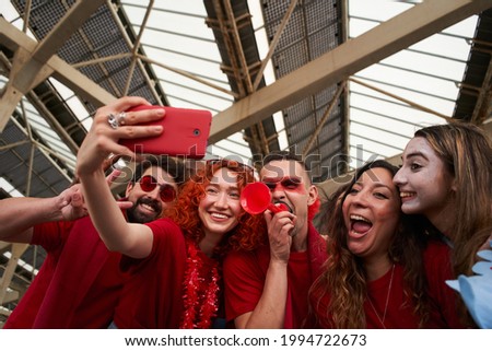 Group of fans take selfie while cheering for their sports team from a stadium. Cheerful male and female fans taking selfie while watching the game at the stadium.