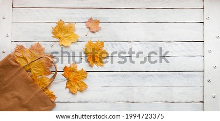 Paper bag with autumn yellow dry leaves on a wooden background. Autumn shopping. Flat layout, top view, copy space