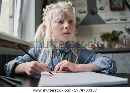 Girl sitting and drawing her picture with calmness at the table at the kitchen