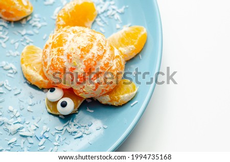 Fruit turtles, a snack made of fresh parts of mandarins served in the shape of water turtles on a blue plate, funny food