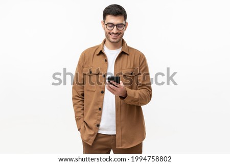 Smiling man wearing casual brown shirt looking at phone, isolated on gray