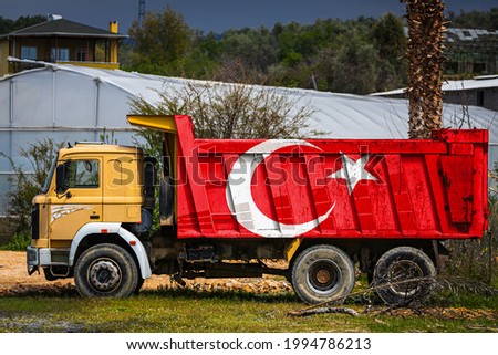 Dump truck with the image of the national flag of Turkey is parked against the background of the countryside. The concept of export-import, transportation, national delivery of goods