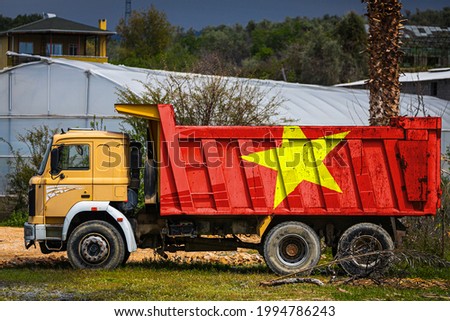 Dump truck with the image of the national flag of Vietnam is parked against the background of the countryside. The concept of export-import, transportation, national delivery of goods