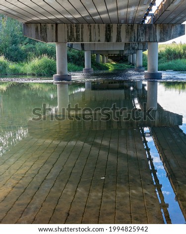 Underneath a concrete bridge built over a shallow rural creek with water reflections