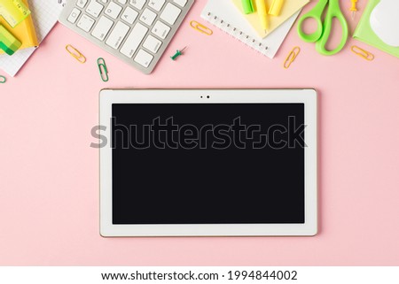 Top view photo of green and yellow stationery organizers pens clips pushpins scissors ruler stickers eraser keyboard mouse and tablet computer on isolated pastel pink background with blank space