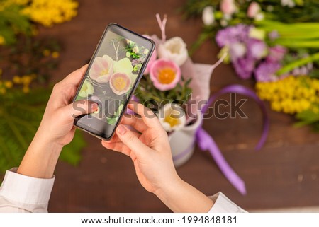 The girl florist takes pictures on the phone of a flower arrangement standing on a wooden background. Opening of the flower business
