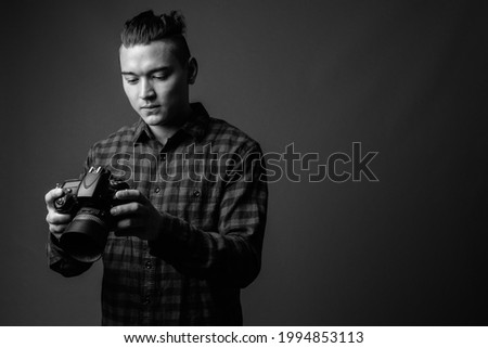 Studio shot of young handsome multi ethnic man wearing checkered shirt against gray background in black and white