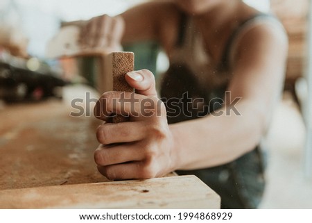 Female carpenter smoothing the lumber with a sanding disc