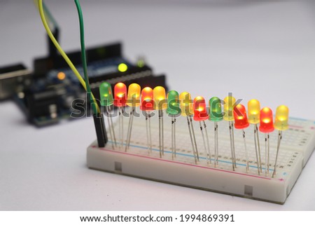 Glowing light emitting diode in short LED which is an Electronic component connected to breadboard with some micro controller on background Royalty-Free Stock Photo #1994869391