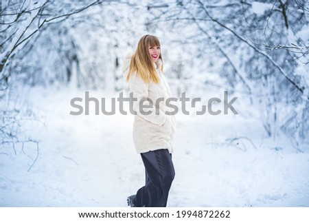 Beautiful smiling confident young white woman pretty face in a white fur coat looking at camera posing alone at snowy forest